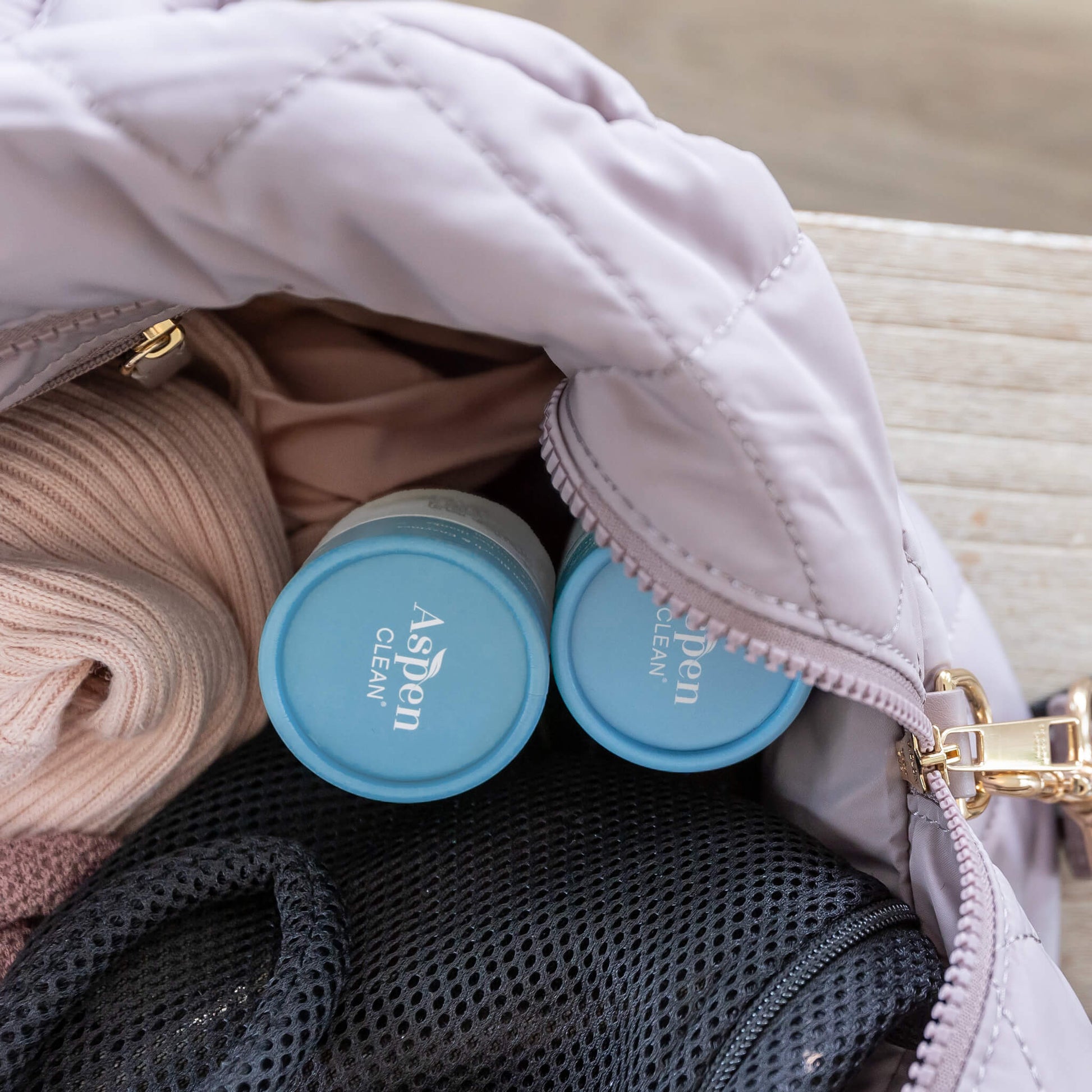 AspenClean laundry detergent pods travel size in a pink travel bag with clothes.